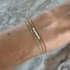 Joli bracelet extrêmement fin composé de trois chaines plus ou moins travaillées en acier inoxydable de couleur or. Nous pouvons également apercevoir une série de parfaites petites perles d'eau douce véritable