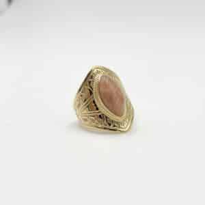 Bague large de type chevalière fabriquée en acier inoxydable de couleur dorée. Sertie en son centre d'une goutte en pierre naturelle de couleur rose pâle