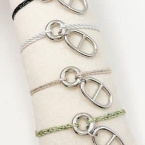 Joli bracelet à cordon tressé composé d'un fin cordon avec lurex scintillant. Nous pouvons également apercevoir un pendentif de forme ronde ainsi qu'une breloque grain de café de couleur argentée 