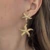 Boucles d'oreilles pendantes en acier inoxydable de couleur dorée composées de deux étoiles de mer