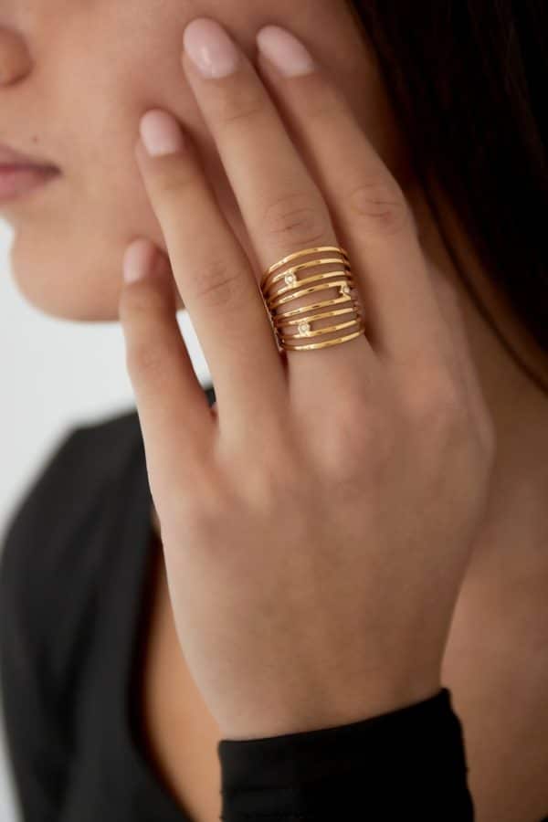 Bague très large sur le doigt composée d'une multitude de fins anneaux et de deux jolis strass blancs