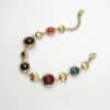 Bracelet assez large en acier inoxydable doré composé d'une ribambelle de strass multicolores et de breloques en acier inoxydable doré