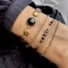 Bracelet assez large en acier inoxydable doré composé d'une ribambelle de strass dans les ton de noir et gris et de breloques en acier inoxydable doré