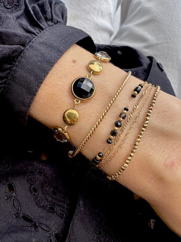 Bracelet assez large en acier inoxydable doré composé d'une ribambelle de strass dans les ton de noir et gris et de breloques en acier inoxydable doré
