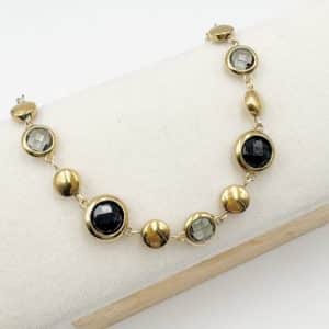 Bracelet assez large en acier inoxydable doré composé d'une ribambelle de strass dans les ton de noir et gris et de breloques en acier inoxydable doré