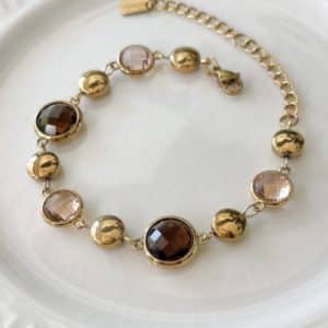 Bracelet assez large en acier inoxydable doré composé d'une ribambelle de strass dans les tons marron beige et de breloques en acier inoxydable doré– Bijou en acier inoxydable