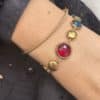 Bracelet assez large en acier inoxydable doré composé d'une ribambelle de strass multicolores et de breloques en acier inoxydable doré