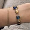 Bracelet assez large en acier inoxydable doré composé d’une ribambelle de strass dans les tons de bleu et de breloques en acier inoxydable doré– Bijou en acier inoxydable Joli bracelet assez large en acier inoxydable doré composé d’une ribambelle de strass dans les tons bleus beige et de breloques en acier inoxydable doré