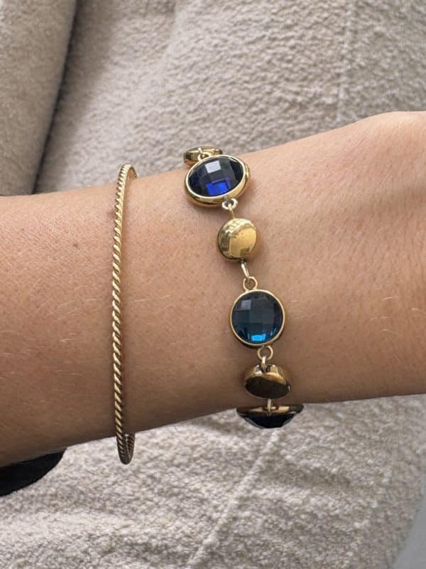 Bracelet assez large en acier inoxydable doré composé d’une ribambelle de strass dans les tons de bleu et de breloques en acier inoxydable doré– Bijou en acier inoxydable Joli bracelet assez large en acier inoxydable doré composé d’une ribambelle de strass dans les tons bleus beige et de breloques en acier inoxydable doré