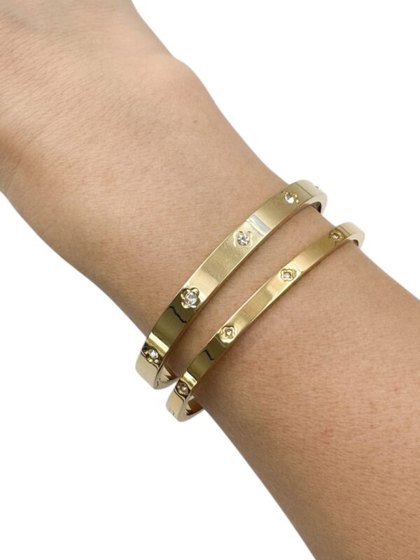 Bracelet jonc en fin en acier inoxydable doré serti de petits strass blanc au centre de trèfles gravés