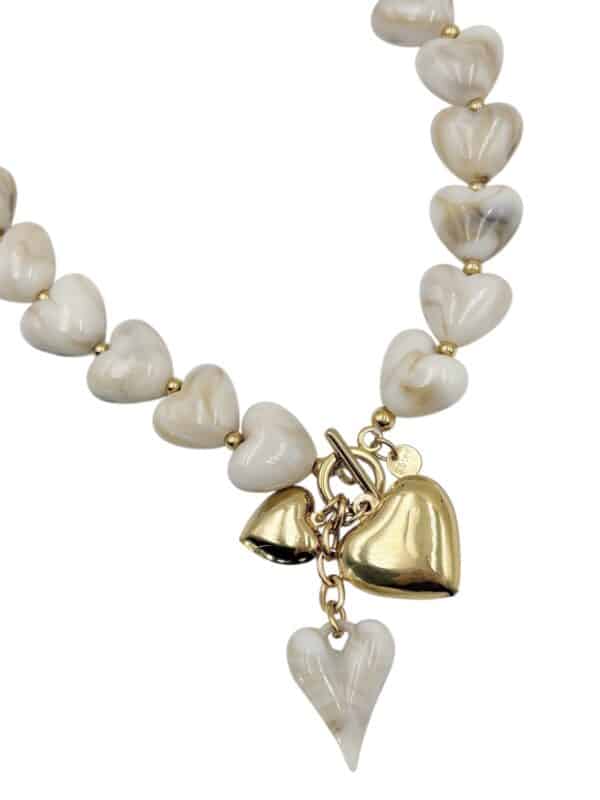 Collier composé d’une succession de coeurs en résine beige avec pampilles en forme de coeurs en résine et acier inoxydable